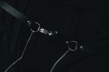 Siyah deri kölelik teçhizatı, siyah kumaş arka planında zincirler..