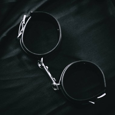 Koyu renk kumaş yüzeyinde metal zincirli siyah deri kelepçeler..