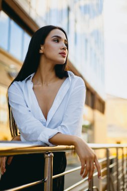 Beyaz gömlekli, kentin balkonunda poz veren kendinden emin Asyalı genç bir kadın..