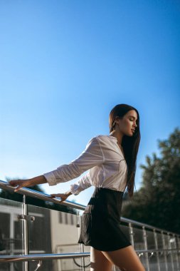 Beyaz tişörtlü, siyah etekli, dışarıda demiryolu kenarında poz veren beyaz bir kadın..