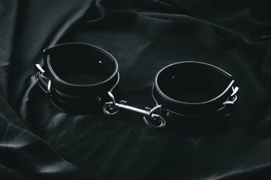 Siyah deri kelepçeler koyu saten kumaş arka planda..