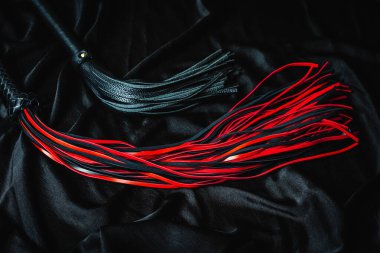 Siyah ve kırmızı deri kırbaçlar koyu kumaş arka planda.