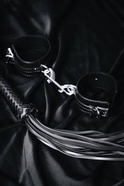 Siyah deri kelepçeler ve siyah kumaş yüzeyinde kırbaç..