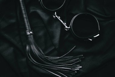 Koyu arkaplanda siyah deri kamçı ve kelepçe - bdsm aksesuarları görüntüleme.