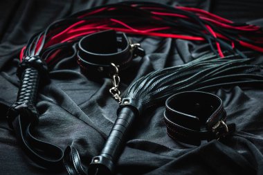 Siyah ve kırmızı deri kamçı ve siyah kumaş yüzeyinde kelepçeler..