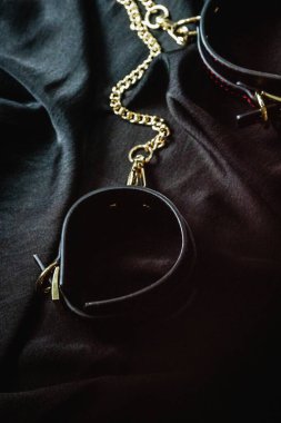 Siyah deri kelepçeler, altın zincirli koyu renk kumaş arka plan..