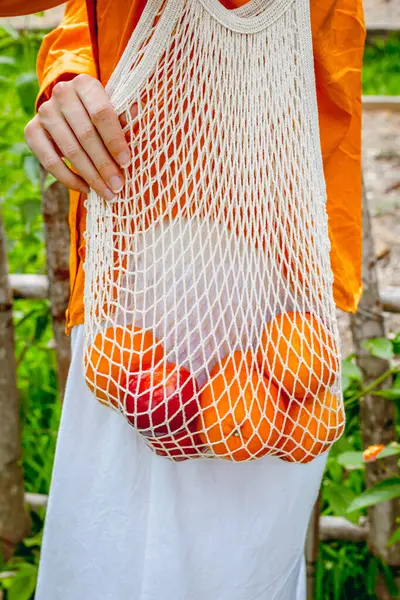 Elinde taze portakal ve elma tutan kişi..