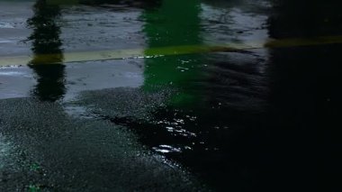 Geceleyin geçen araba ışıklarıyla şehir asfaltına yağan yağmur yansımaları