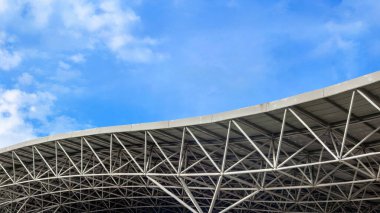 Mavi gökyüzüne karşı kıvrımlı çelik çatı yapısı.