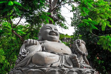 Gülümseyen Buda heykeli açık havada yemyeşil yeşillikler arasında.