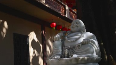 Güneşli gölgelerde gülümseyen Buda ve kırmızı fenerlerle huzurlu bir avlu.