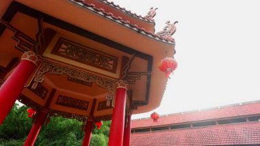 Yeşilliğin ortasında süslü çatı ve kırmızı fenerlerle süslü geleneksel mimari.