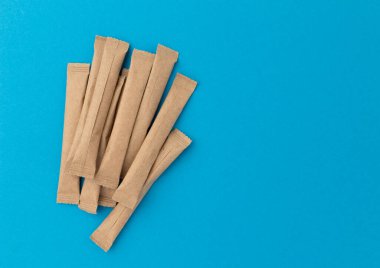 beige sticks of sugar with space for text on blue background, flat lay, top view