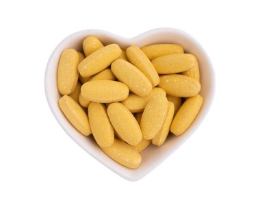 Seramik kasede vitamin hapları var. Kalp şekli beyaz arka planda izole edilmiş. Kırpma yolu, üst görünüm, sağlık takviyesi, düz yatak.