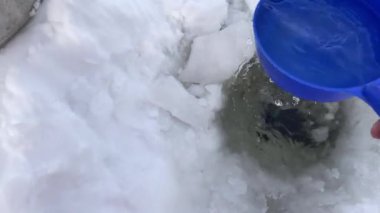 Pallas Yllastunturi Ulusal Parkı, Laponya, Finlandiya 'daki donmuş bir göldeki bir delikten su toplayan adam.