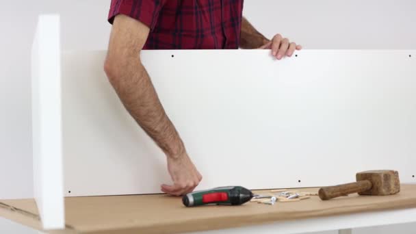 一个穿着黑色裤子和红色格子衬衫的木匠正在组装一个白色的书架 Uhd — 图库视频影像