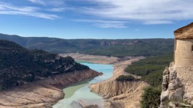 La Pertusa Kilisesi, Lleida, İspanya 'da kurak bir arazi manzaralı vadi ve rezervuara bakan tarihi bir binayı gözler önüne seriyor..