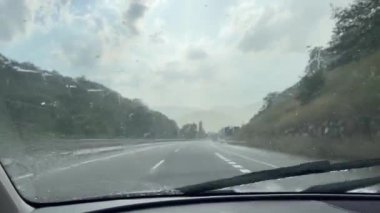 Olot, Pyrenees, İspanya 'da bir otoyolda yağmurlu bir gün ön camında yağmur damlaları olan bir arabanın içinden izleniyor..