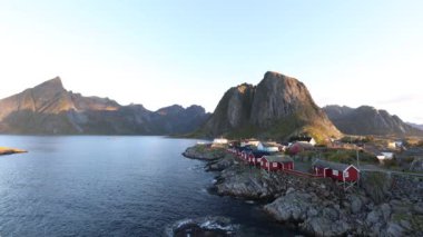 Kuzey Norveç 'te Hamny, Lofoten Adaları' nda gündoğumu, kıyı şeridi boyunca geleneksel kırmızı evler ve dramatik dağlarla.