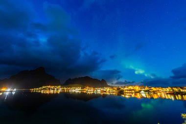 Kuzey Işıkları Reine üzerinde, Lofoten Adaları, Kuzey Norveç, gökyüzünü şehrin üzerinde canlı renklerle aydınlatıyor..