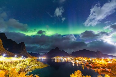 Kuzey Işıkları Reine üzerinde, Lofoten Adaları, Kuzey Norveç, gökyüzünü şehrin üzerinde canlı renklerle aydınlatıyor..