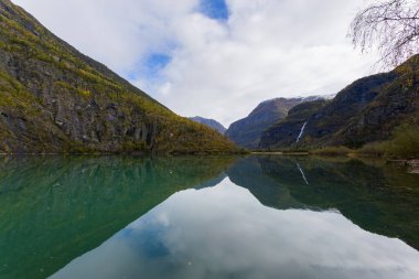 Autumn landscape in Skjolden, Norway, with a calm lake reflecting the mountains and colorful foliage. clipart