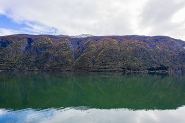 Norveç 'in Lustrafjorden kentindeki sonbahar manzarasında berrak su yansımaları, dağlar ve renkli yeşillikler yer almaktadır..