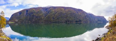 Autumn landscape in Lustrafjorden, Norway, featuring clear water reflections, mountains, and colorful foliage. clipart