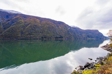 Autumn landscape in Lustrafjorden, Norway, featuring clear water reflections, mountains, and colorful foliage. clipart