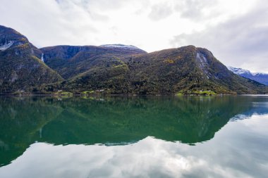 Norveç 'in Lustrafjorden kentindeki sonbahar manzarasında berrak su yansımaları, dağlar ve renkli yeşillikler yer almaktadır..