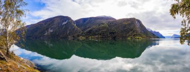 Norveç 'in Lustrafjorden kentindeki sonbahar manzarasında berrak su yansımaları, dağlar ve renkli yeşillikler yer almaktadır..