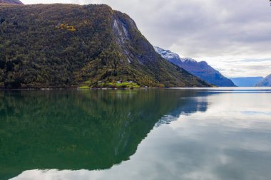 Norveç 'in Lustrafjorden kentindeki sonbahar manzarasında berrak su yansımaları, dağlar ve renkli yeşillikler yer almaktadır..