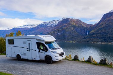 Norveç 'teki sakin Lustrafjorden' in yanında park etmiş bir karavan. Arka planda çarpıcı dağlar ve şelale var..