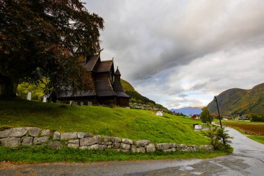 Hopperstad Stavkyrkje in Norway, a historic wooden church surrounded by autumn trees and a peaceful graveyard. clipart