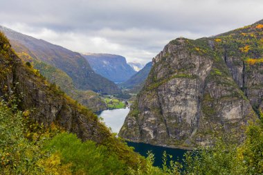 View of the Hagatunnel road in Steine, Norway, with dramatic cliffs, green fields, and autumn colors. clipart