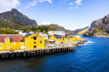 Norveç, Lofoten Adaları 'ndaki Nusfjord manzaralı, kırmızı ve sarı ahşap evler, tekneler ve kristal berrak sularla.