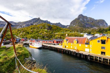 Norveç, Lofoten Adaları 'ndaki Nusfjord manzaralı, kırmızı ve sarı ahşap evler, tekneler ve kristal berrak sularla.