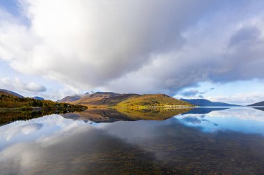 Autumn landscape of Senja Island, Norway, with colorful trees, serene water reflections, and dramatic mountains. clipart