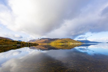 Norveç, Senja Adası 'nın sonbahar manzarası. Renkli ağaçlar, dingin su yansımaları ve dramatik dağlar..