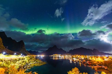 Kuzey Işıkları Reine üzerinde, Lofoten Adaları, Kuzey Norveç, gökyüzünü şehrin üzerinde canlı renklerle aydınlatıyor..