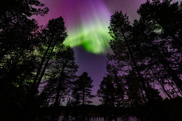 Northern lights in Kiruna, Sweden, reflecting on calm water in September with stars and forest.