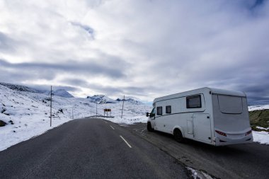 Norveç 'in güneyindeki Sognefjellsvegen yolunda karla kaplı dağlar ve manzaralı manzaralarla çevrili bir karavan..