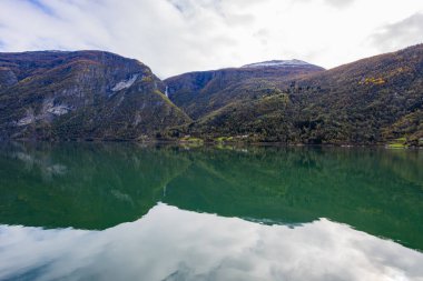 Norveç 'in Lustrafjorden kentindeki sonbahar manzarasında berrak su yansımaları, dağlar ve renkli yeşillikler yer almaktadır..