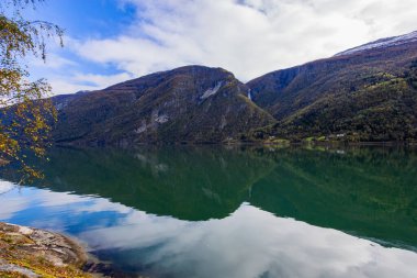 Autumn landscape in Lustrafjorden, Norway, featuring clear water reflections, mountains, and colorful foliage. clipart