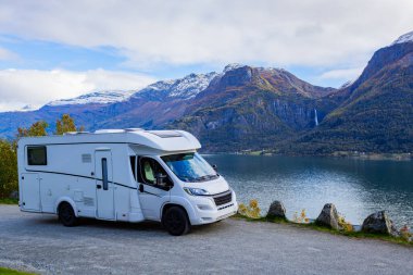 Norveç 'teki sakin Lustrafjorden' in yanında park etmiş bir karavan. Arka planda çarpıcı dağlar ve şelale var..