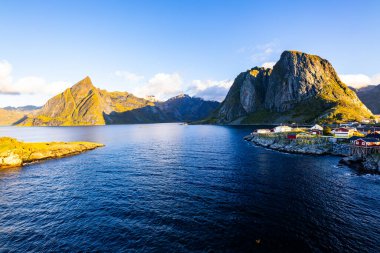 Norveç 'in Hamnoy, Lofoten Adaları' nda gün doğumu, kıyı şeridi boyunca geleneksel kırmızı evler ve dramatik dağlar..