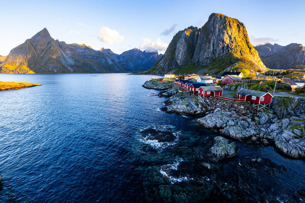 Sunrise over Hamnoy, Lofoten Islands, Norway, with traditional red houses and dramatic mountains along the coastline.