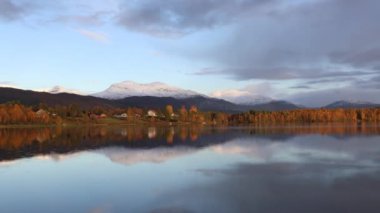 Kuzey Norveç 'in sonbahar manzarası, renkli ağaçlar, dingin su yansımaları ve dramatik dağlar..