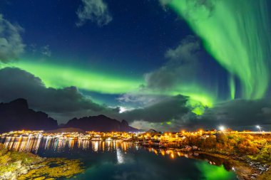 Kuzey Işıkları Reine üzerinde, Lofoten Adaları, Kuzey Norveç, gökyüzünü şehrin üzerinde canlı renklerle aydınlatıyor..