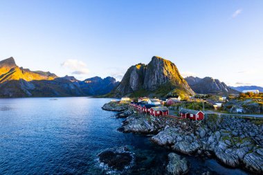 Norveç 'in Hamnoy, Lofoten Adaları' nda gün doğumu, kıyı şeridi boyunca geleneksel kırmızı evler ve dramatik dağlar..